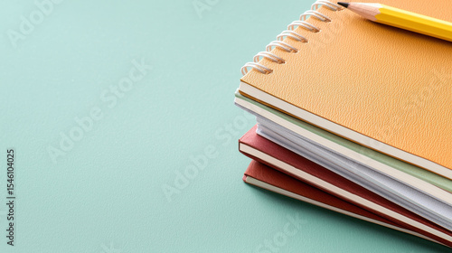 Stack of colorful notebooks with yellow pencil on mint green background, creating cheerful and organized workspace