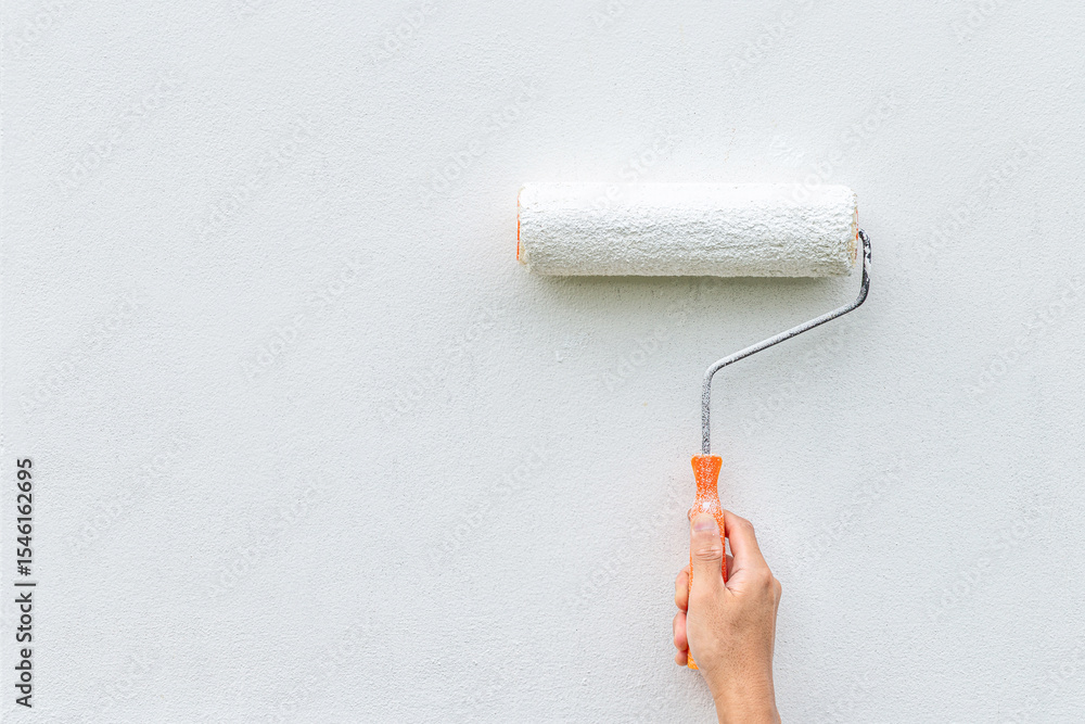 Obraz premium Hand painting white wall with paint roller, close-up shot showing DIY home improvement or renovation.