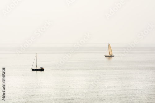 Two sailboats are sailing in the ocean, one is closer to the shore