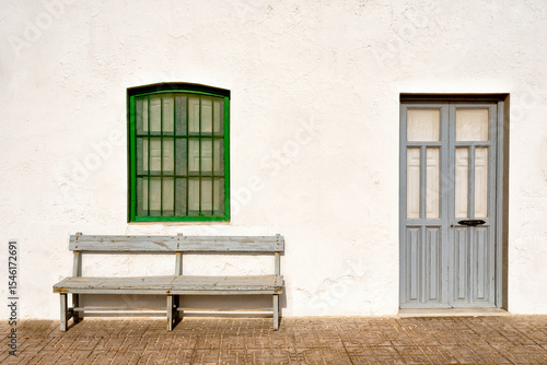 A whitewashed white building with a green window over a gray bench and door. Cabo de Gata.