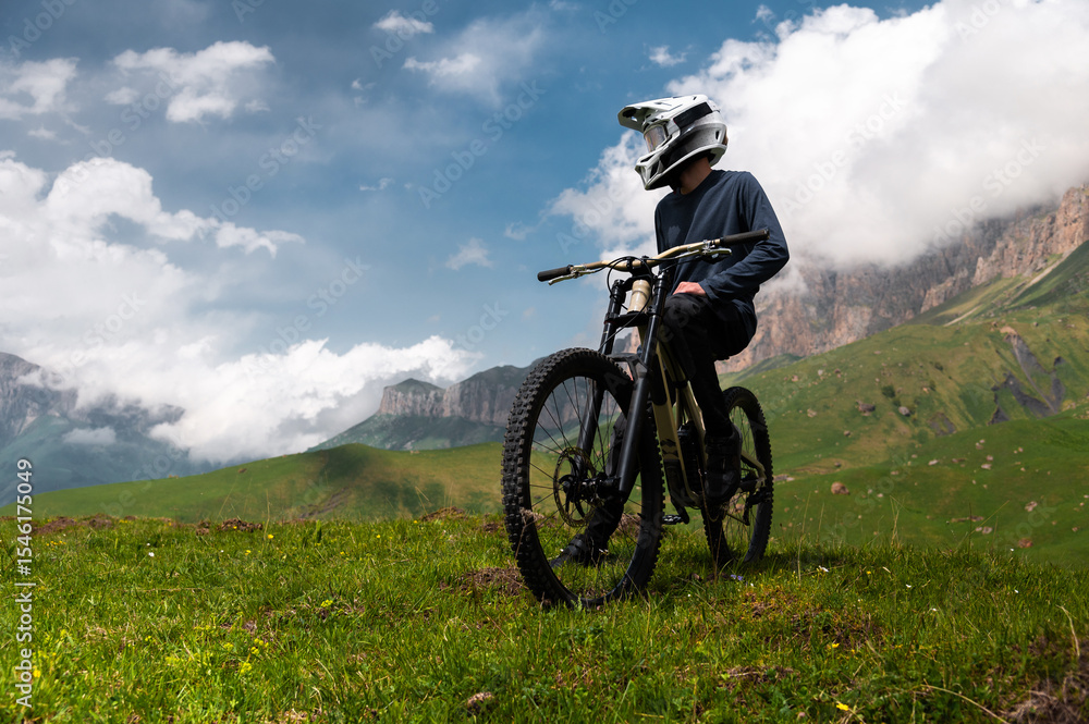 Rider cyclist man wearing mask and full face helmet standing on his bike on top of hill high in mountains. Space copy background for mountain biking Rider cyclist man wearing mask and full face helmet standing on his bike on top of hill high in mountains. Space copy background for mountain biking