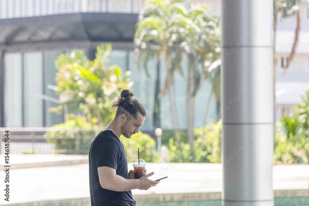 Fototapeta premium An attractive fitness male trainer is taking a refreshment drink and checking his online exercise application on smartphone, Young and handsome man with technology