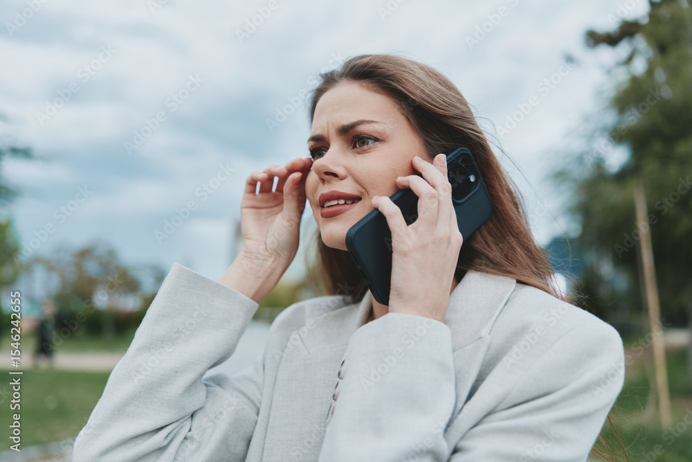 Professional businesswoman talking on the phone outdoors, expressing concern while wearing a light suit in a vibrant natural setting. Professional businesswoman talking on the phone outdoors, expressing concern while wearing a light suit in a vibrant natural setting.