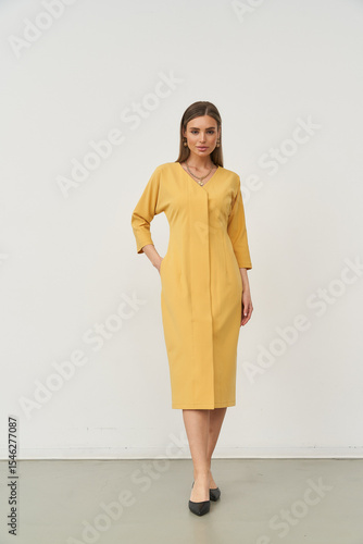 Stylish female model poses in a chic mustard dress in a minimalist studio