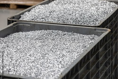 Two grey industrial bins are filled to the brim with shiny, fine metal shavings, indicative of a manufacturing process within a factory