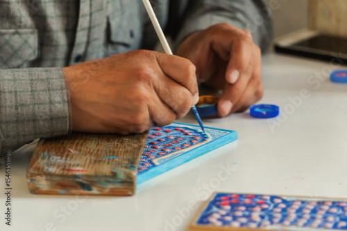 Uzbek artist hand-painting traditional ceramic tile with floral design in Samarkand, Uzbekistan