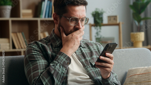 Bilde på lerret Caucasian adult man male guy at home living room nervous looking at mobile phone