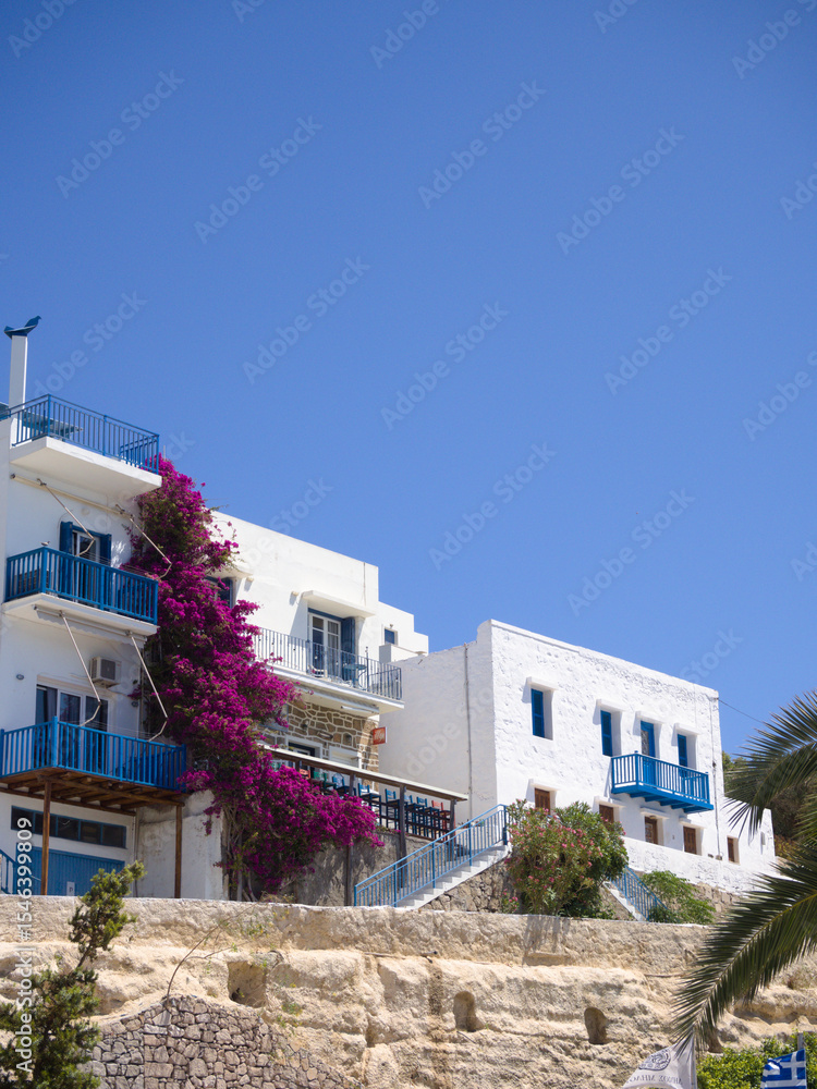 Fototapeta premium Elevated view of charming facades in Adamas, Greece with bright sky and vibrant pink flowers.