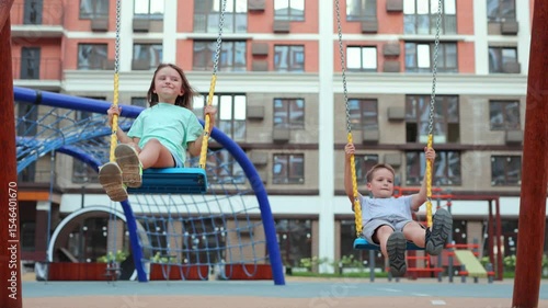 Happy children, boys and girls, ride on a swing on a modern playground.