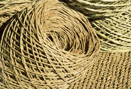 Natural raffia fibers are wound into spools against a crocheted background. The spools are beige and craft colors.