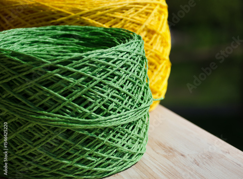 Natural raffia fibers are wound into spools against a background of green grass.