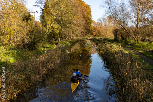Two people in a kayak paddle down a beautiful stretch of the River Wey Navigation canal in Autumn
