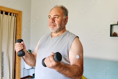 Mature man with diabetes and continuous glucose monitor on his arm making sport exercises at home