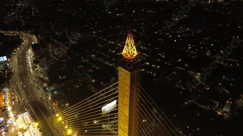 Aerial tilt view of illuminated Rama VIII Bridge at night. Cable-stayed bridge crossing Chao Phraya River in Bangkok, Thailand, 4k