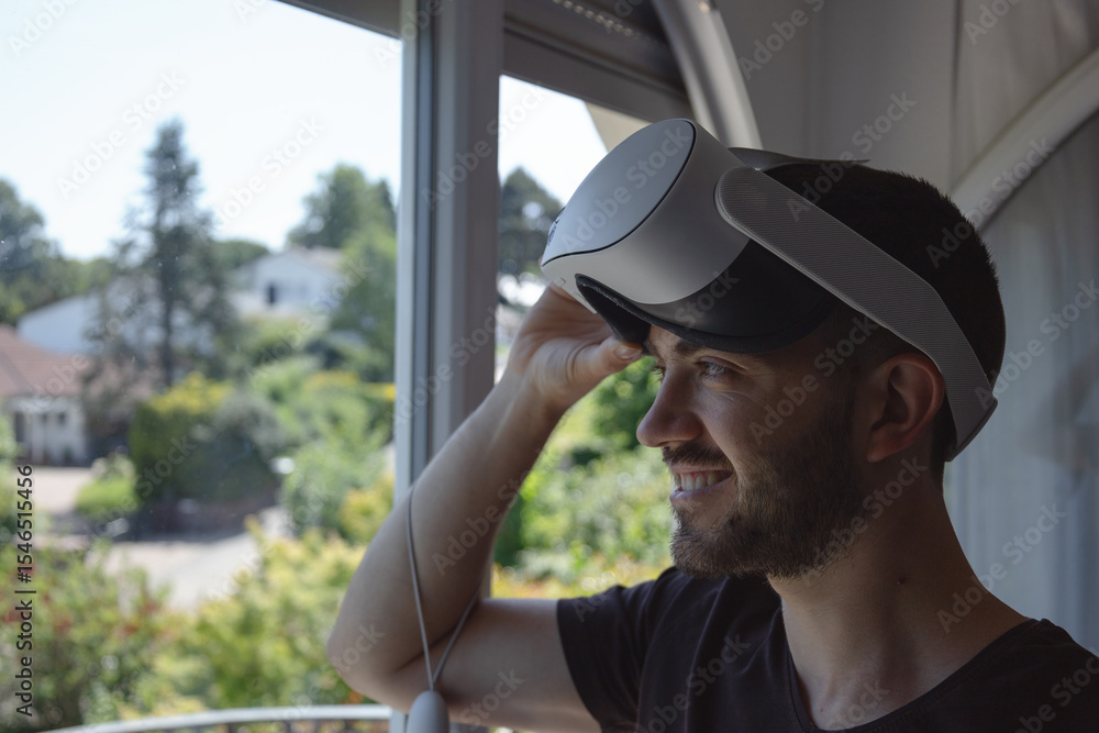 Obraz premium Young Man in a casual tshirt using virtual reality glasses, wearing new generation vr headset. looking into the window and smiling.
