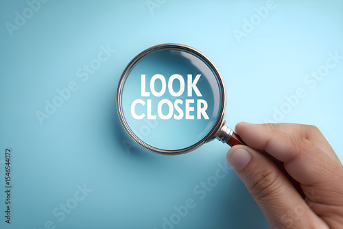 Hand holding magnifying glass showing look closer text on blue background