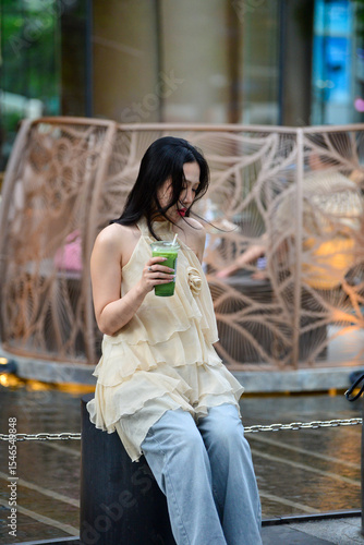 Elegant Woman Holding Matcha Green Tea with Wind Blown Hair Outdoors