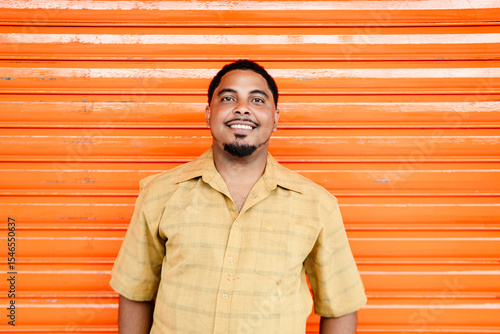 Smiling dominican man posing in front of orange wall