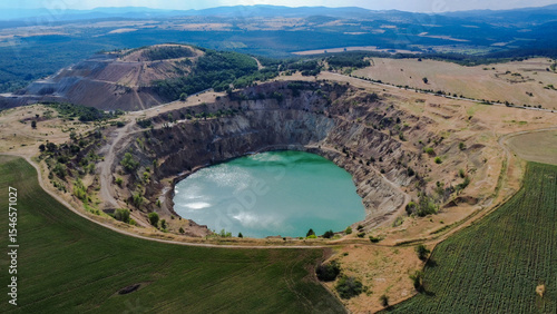 Aerial view of Tsar Asen Mine, Bulgaria – a former open-pit mine now filled with striking turquoise water. The steep terraced slopes and surrounding fields reflect the site's industrial past and natur
