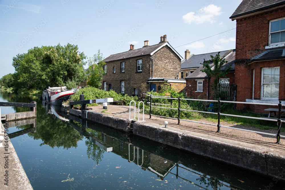 Fototapeta premium Enfield Lock on a sunny day, showcasing the historic canal lock gates, calm waters, and surrounding greenery in bright, clear weather.