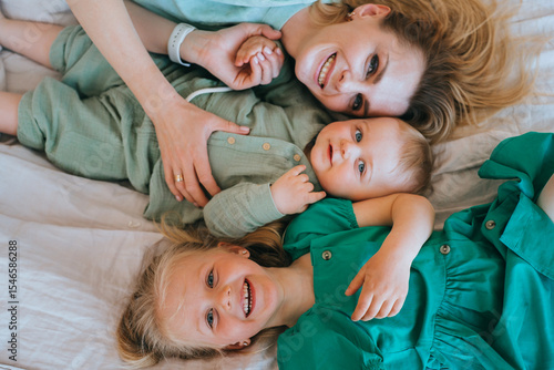 фотографія A mother joyfully embraces her two children on a bed, capturing a heartfelt moment of affection and familial warmth in a serene environment