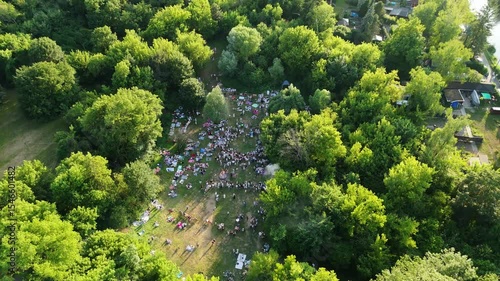 Aerial view of a field where the traditional Slavic festival of Ivan Kupala is celebrated, surrounded by dense forest. People gather in a circle, with bonfires and folk rituals taking place in a vibra