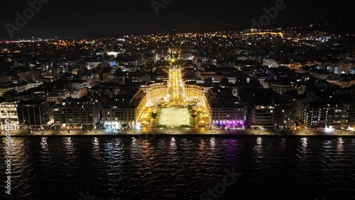 Aerial night view of Thessaloniki, Greece, captured by drone. Illuminated landmarks, city lights, and waterfront in cinematic 4K quality.