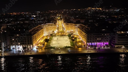 Aerial night view of Thessaloniki, Greece, captured by drone. Illuminated landmarks, city lights, and waterfront in cinematic 4K quality.