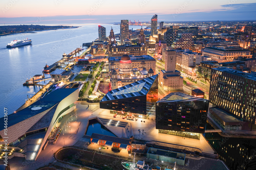 Fototapeta premium Aerial image of Liverpool skyline illuminated by the lights of the evening with a large ferry traveling on river Mersey