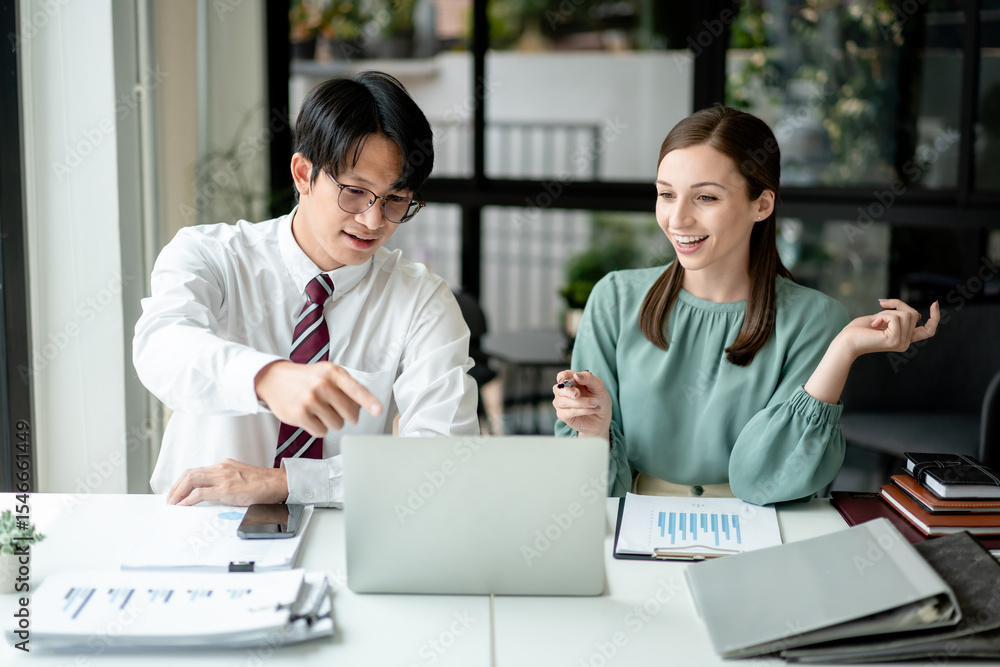 Asian man and European woman working on a laptop discussing business data analytics and financial charts in office for planning strategy together Asian man and European woman working on a laptop discussing business data analytics and financial charts in office for planning strategy together