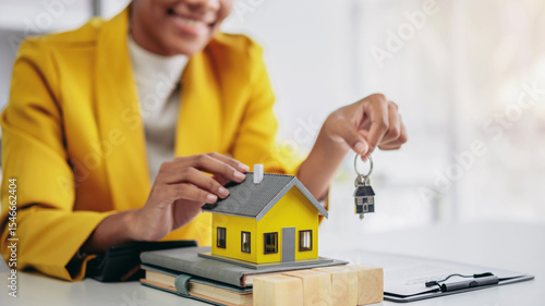 A woman is holding a key and yellow house. The house is a model and the woman is a real estate agent or a homeowner. Concept of loan and insurance