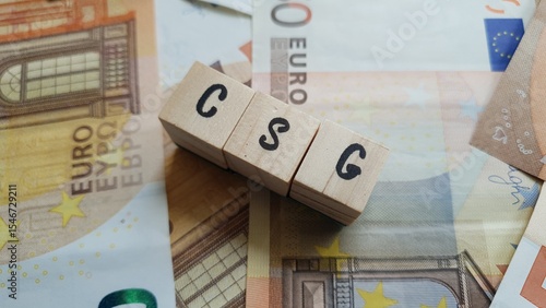 CSG acronym made of wooden letter cubes on pile of Euro banknotes. Contribution Sociale Généralisée (General Social Contribution, a tax funding social security)
