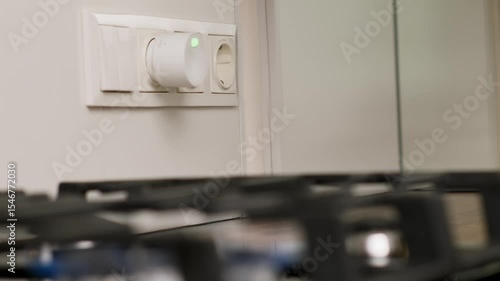 Hand Installing a Compact Gas Detector into Wall Socket Near Kitchen Stove for Safety Monitoring