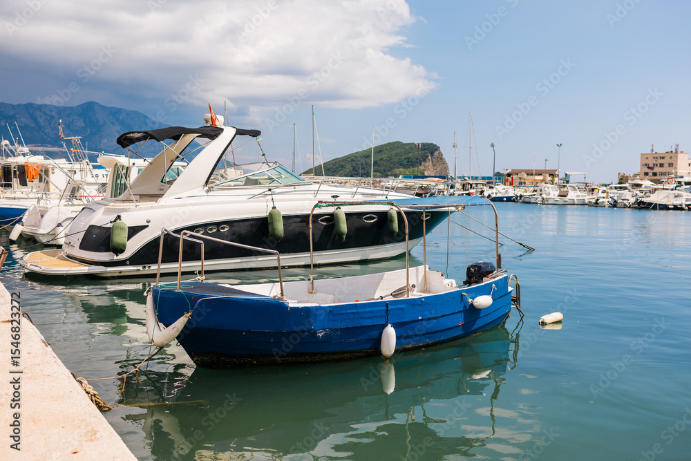 Obraz premium Motorboat moored in scenic marina with mountain background. Coastal lifestyle, nautical leisure, and summer tourism on waterfront.