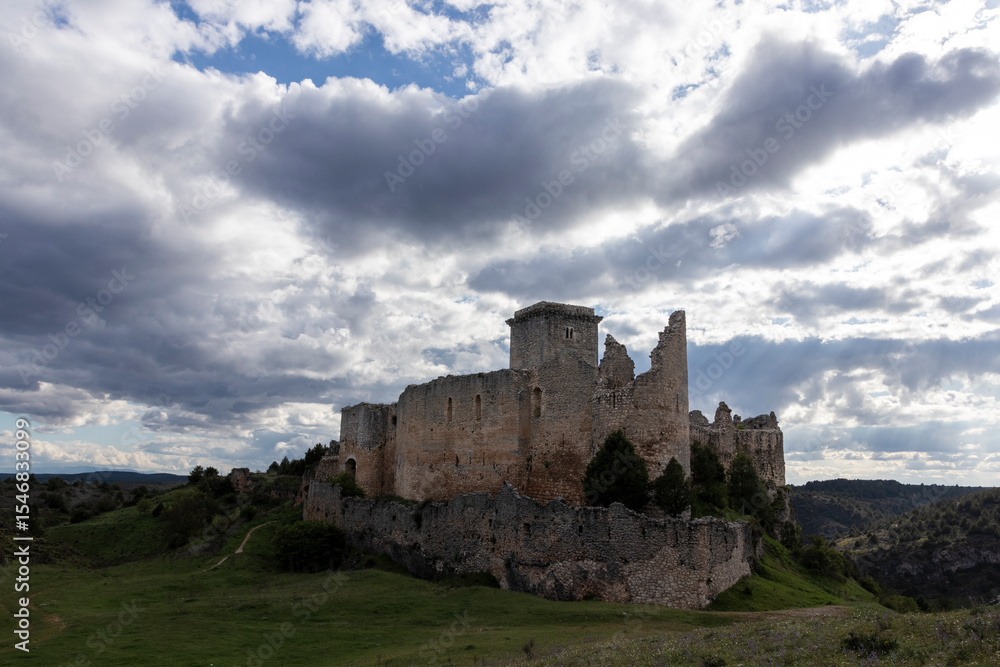 Obraz premium Ruins of rello castle emerging from green hill under cloudy sky