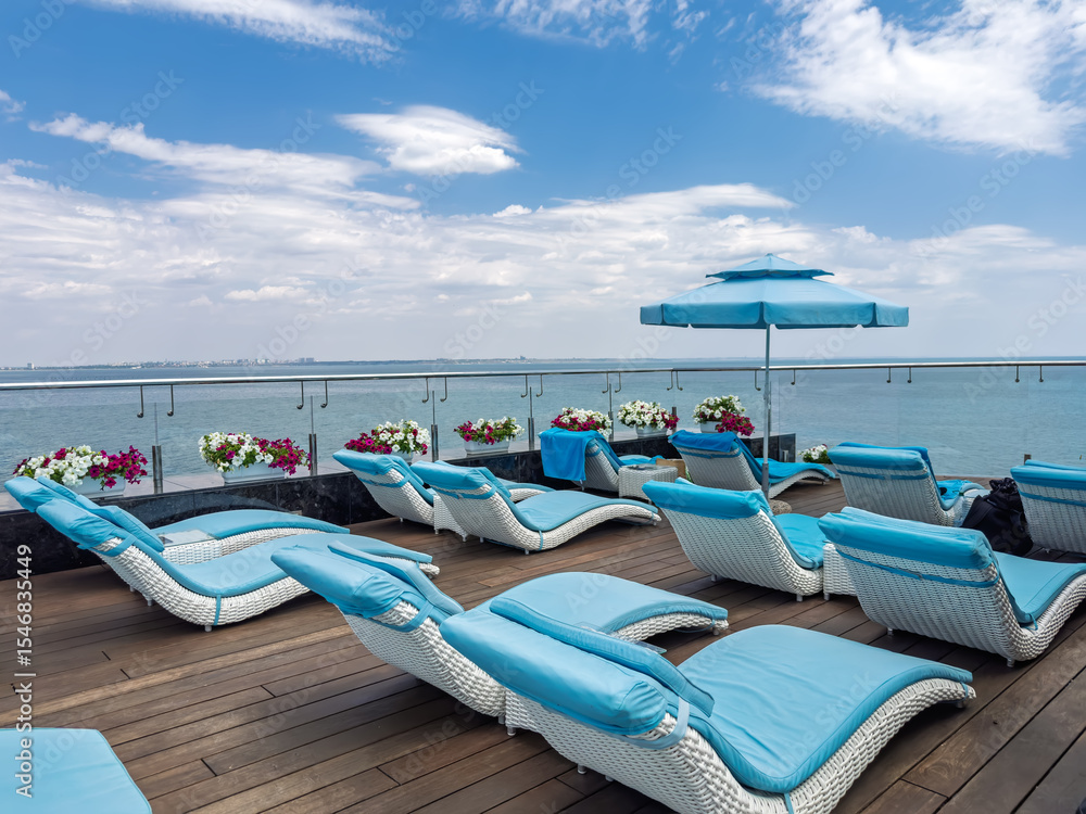Fototapeta premium Idyllic summer vacation scene. Empty lounge chairs on a sundeck overlooking the calm ocean. Concept of travel, escape, and serene holiday.