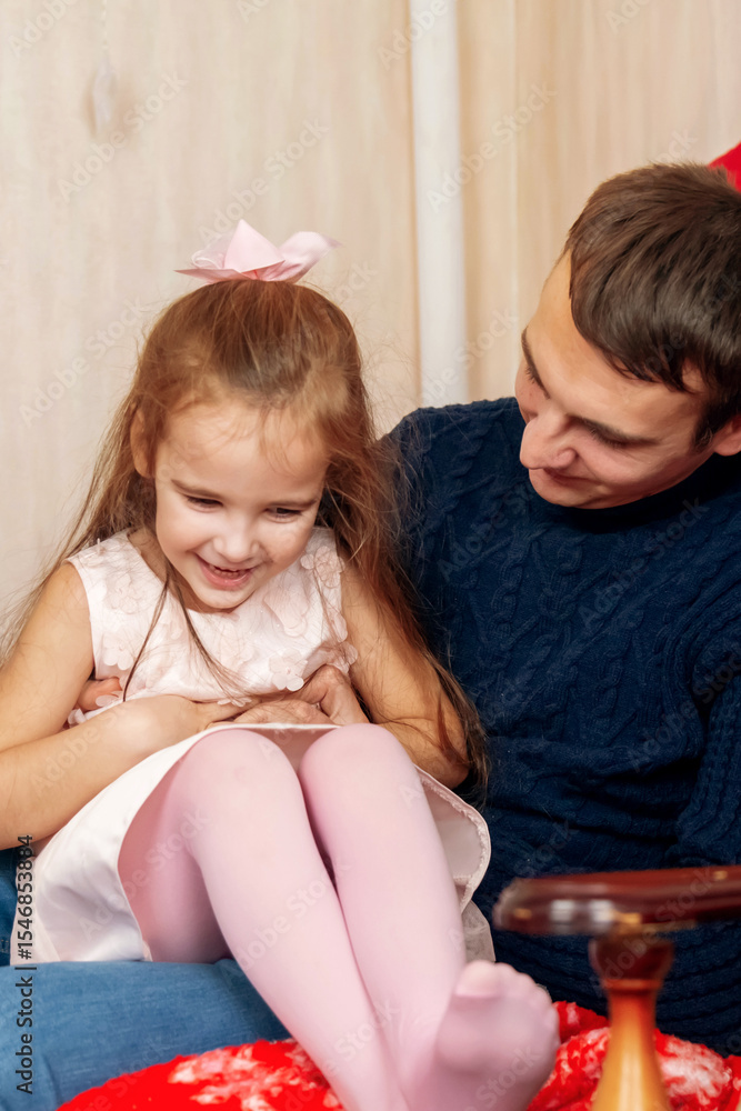 Happy family having fun at home for Christmas. Father tickles her daughter lying on the sofa. Festive cozy interior Happy family having fun at home for Christmas. Father tickles her daughter lying on the sofa. Festive cozy interior