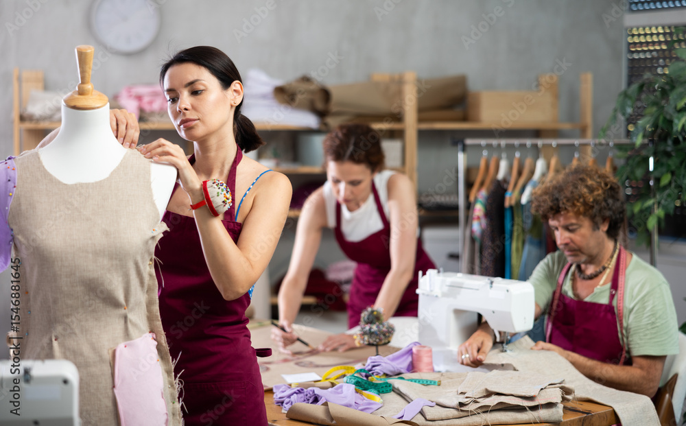 Obraz premium Creative female dressmaker working with mannequin while others sewing and drawing in tailor studio