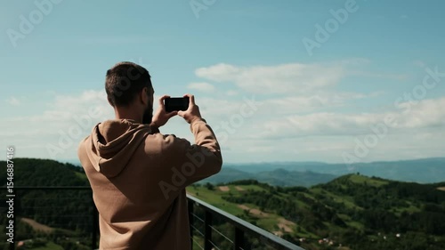 Wallpaper Mural Young man smiling while taking a photo or making video with his smartphone in the Serbian mountains. Male travel blogger. Torontodigital.ca