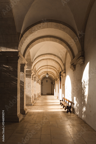 Foto Elegant stone corridor with arched ceilings and benches, bathed in warm sunlight, captures the serene and historic atmosphere of a Lisbon monastery or cloister