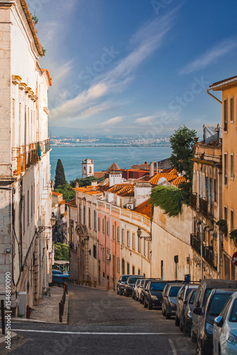 Charming Lisbon street scene featuring colorful buildings, parked cars, and a stunning view of the Tagus River under a bright blue sky, perfect for travel inspiration.