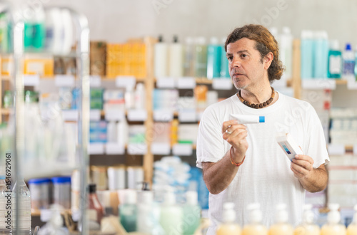 Wall Mural Adult man buyer chooses box of ointment in pharmacy