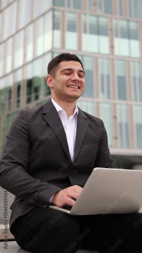 Professional man working on laptop outdoors at a modern office building during a sunny day in the city Professional man working on laptop outdoors at a modern office building during a sunny day in the city