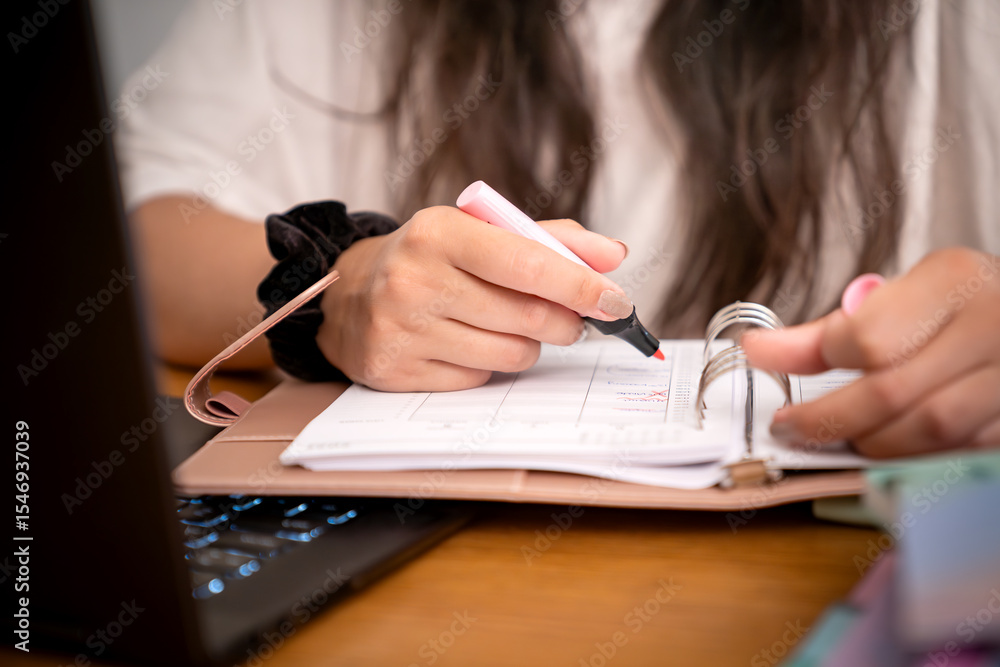 Obraz premium Kobieta robi notatki w kalendarzu przy komputerze