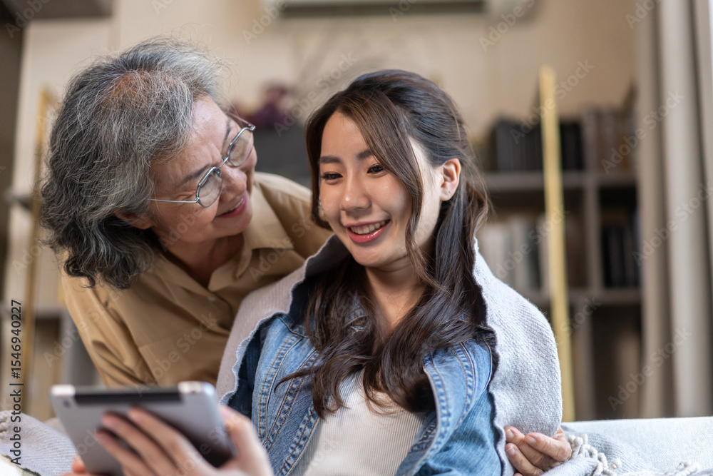 Asian senior mother and daughter smiling and talking using tablet browsing social media, shopping online, watching movies or series, enjoying entertainment digital connection and bonding at home Asian senior mother and daughter smiling and talking using tablet browsing social media, shopping online, watching movies or series, enjoying entertainment digital connection and bonding at home