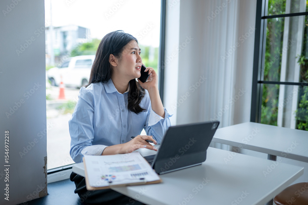 woman is talking on her cell phone while sitting at a desk woman is talking on her cell phone while sitting at a desk