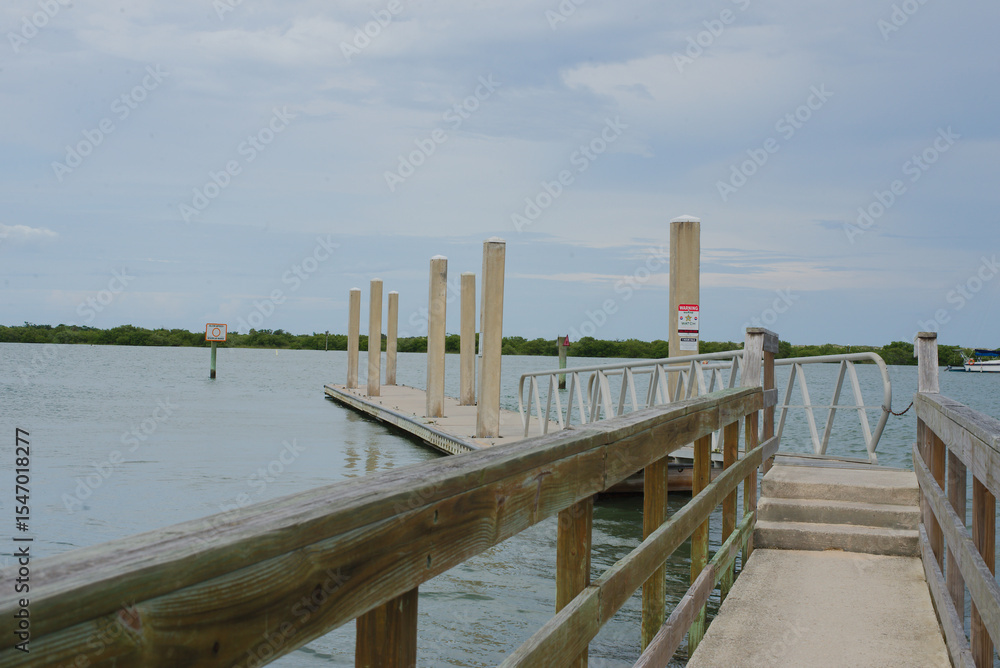 Fototapeta premium Dockside View of Sailboats Anchored on Serene Coastal Waters. A scenic view featuring a dock leading to a calm sea with moored sailboats under a blue sky, invoking feelings of relaxation and tranquili