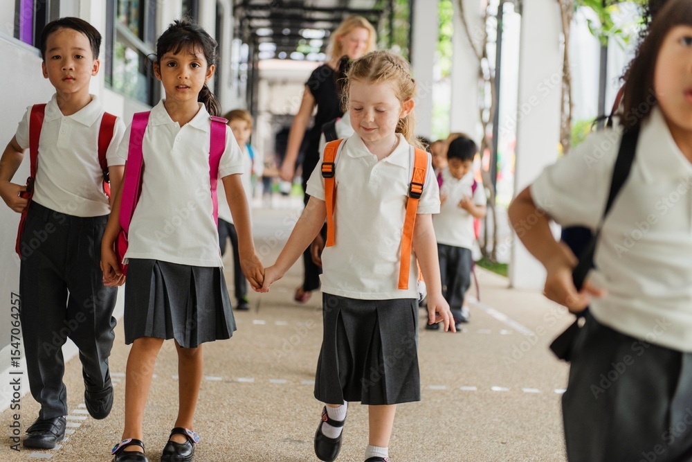 Obraz premium Young children, boys and girls, in school uniforms, walking together. Elementary school uniforms, and school environment. Boys and girls in school uniforms. Diverse kids at elementary school.