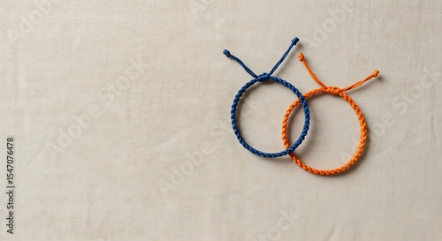 Two woven string bracelets, one blue and one orange, are intertwined on a neutral surface.