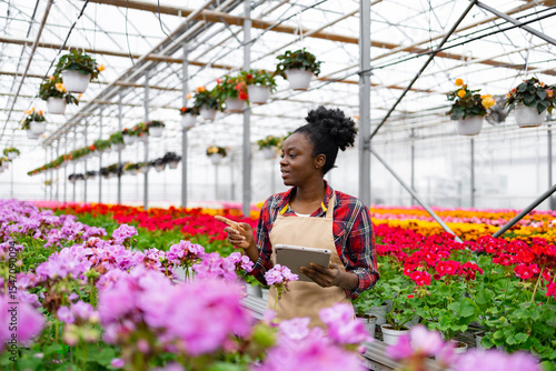 Canvas Print A woman with a tablet gestures in a colorful greenhouse filled with vibrant flowers